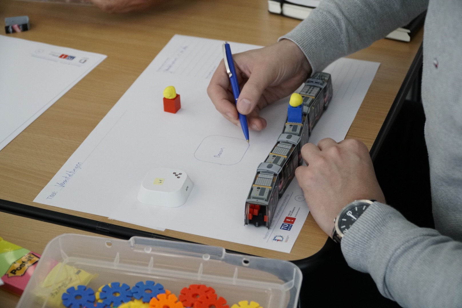 A workshop participant drawing his idea of how to integrate beacons into the public transport system of Vienna.
                  Here, he uses Lego blocks and modeling clay to create workers, where the yellow clay way used for construction site hats.